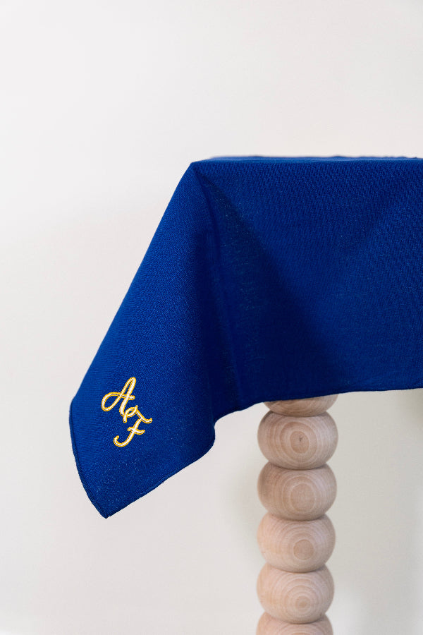 Koningsblauw tafelkleed gepersonaliseerd met een monogram in crèmekleur en gouddraad