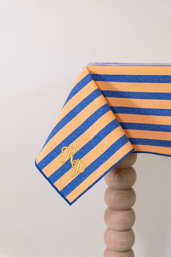 Oranje-blauw gestreept tafelkleed gepersonaliseerd met een monogram in crèmekleur en gouddraad