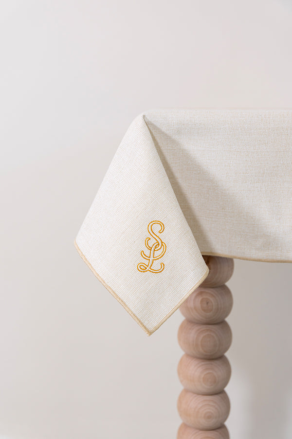 Zachtbeige tafelkleed gepersonaliseerd met een monogram in crèmekleur en gouddraad