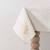 Zachtbeige tafelkleed gepersonaliseerd met een monogram in crèmekleur en gouddraad